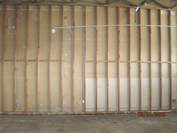 Photo of interior room of a home large wall in an asbesotos remediation project managed by Precision Environmental Services. All drywall and insulation are removed exposing the wall studs.