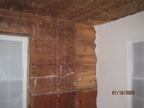 Photo of interior room of a home in an asbesotos removal project overseen by Precision Environmental Services. Wood planking on the wall and ceiling and drywall on the right wall is shown.