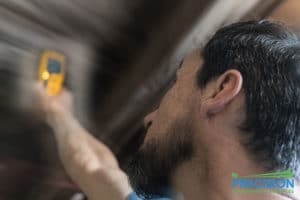 Male mold inspector holding a yellow guage checking for mold by wall